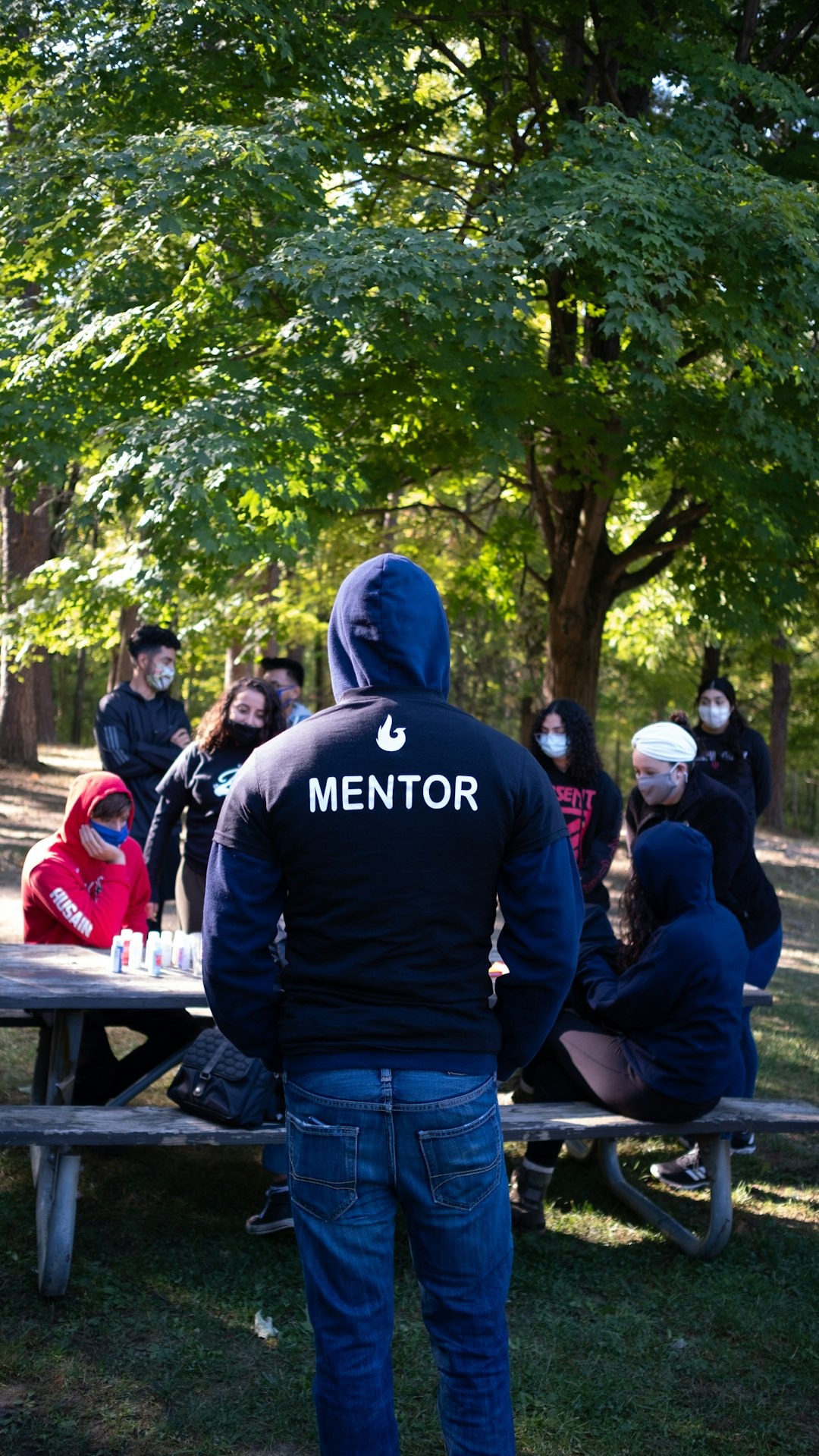 A mentor speaks to a diverse group at an outdoor table.