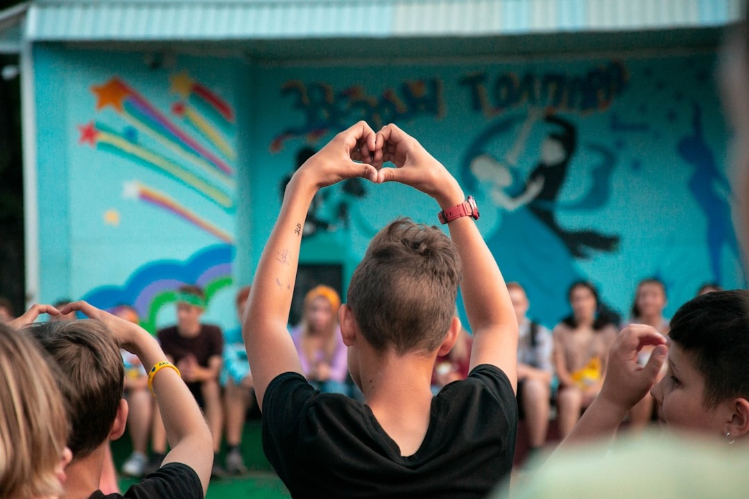 Young person makes a heart shape with their hands at an event.
